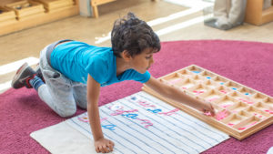 a boy sitting on a pink rug arranges wooden letters on a rug