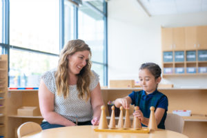 a teacher sits at a wooden table and looks at a young girl