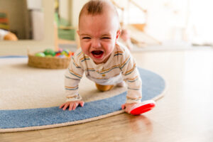 Baby is crying, crawling on a cream and blue rug